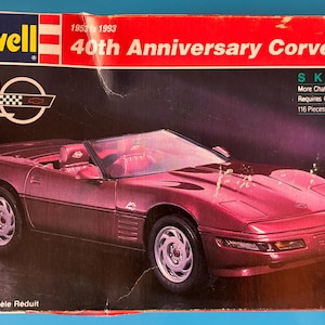 Könnte beinhalten: Modellbausatz-Box mit einem weinroten 40th Anniversary Corvette Cabrio. Die Box hat das Revell-Logo und Text, der darauf hinweist, dass Kleber benötigt wird und 116 Teile enthält. Die Box hat auch den Text "Model Kit Modèle Réduit" und den Maßstab 1:24.