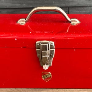 May include: A red metal toolbox with a silver handle and latch. The toolbox has a brand name on the front.