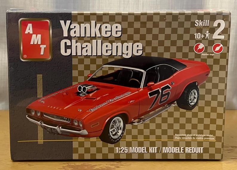 Op de afbeelding: Een 1:25 schaalmodelkit van een rode Dodge Challenger met een zwart dak en het nummer 76 aan de zijkant. De doos heeft de tekst "Yankee Challenge" en "Skill 2".