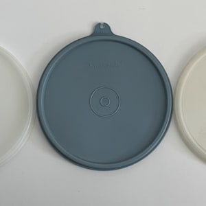 Puede incluir: Tres tapas redondas de plástico, una blanca, una gris claro y una gris oscuro.