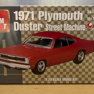 Op de afbeelding: Een modelbouwdoos voor een 1971 Plymouth Duster Street Machine. De doos heeft een rood 1971 Plymouth Duster model op een geruite achtergrond. De doos is gelabeld met "Skill 2, 10+ jaar".
