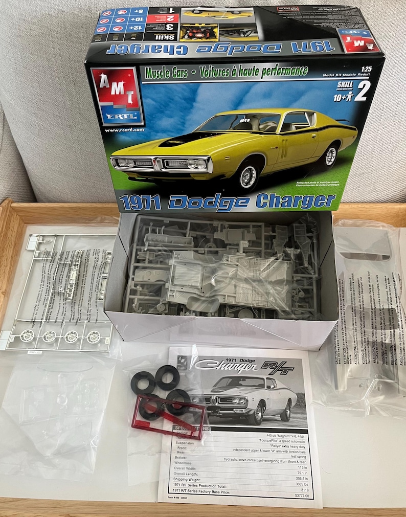 Puede incluir: Un kit de maqueta de un Dodge Charger R/T de 1971 en amarillo con rayas negras. La caja incluye las piezas del coche, las instrucciones y una hoja de calcoman&iacute;as. La caja est&aacute; etiquetada con "1971 Dodge Charger" y "Muscle Cars - Voitures &agrave; haute performance".