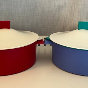 以下が含まれることがあります： 蓋付きのカラフルなサービング皿が2つ。1つは赤色で白い蓋と赤いハンドルが付いています。もう1つは青色で白い蓋と青いハンドルが付いています。どちらも蓋の上に正方形のハンドルが付いています。サイズはcmです。