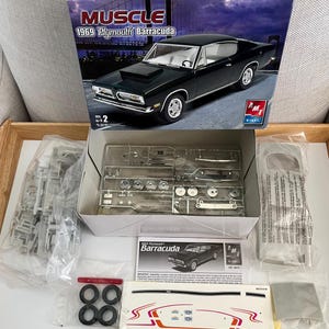 Puede incluir: Un kit de maqueta de un Plymouth Barracuda 1969 en verde. La caja muestra el coche en una foto en blanco y negro. El kit incluye piezas, instrucciones y calcoman&iacute;as. La caja est&aacute; etiquetada como "Muscle".