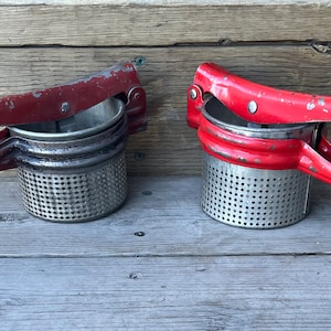 May include: Two red metal potato mashers with a stainless steel mesh strainer. The mashers are in a used condition with some rust and scratches.