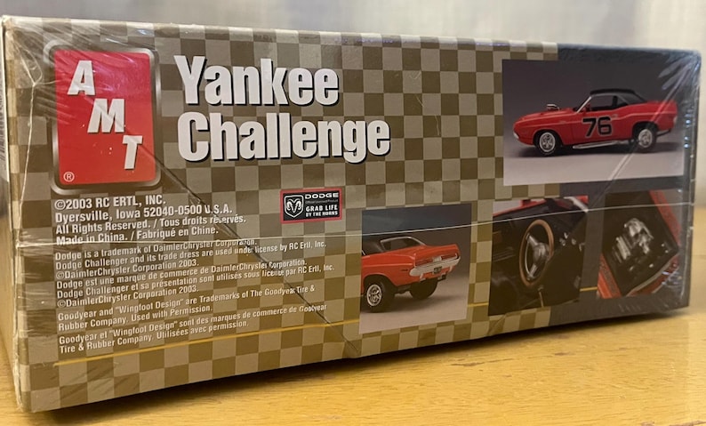 Op de afbeelding: Een modelbouwdoos voor een rode Dodge Challenger Yankee Challenge uit 1970. De doos bevat afbeeldingen van de auto, waaronder een close-up van de motor en het interieur. De doos bevat ook de tekst "Yankee Challenge" en "Dodge Grab Life by the Horns".