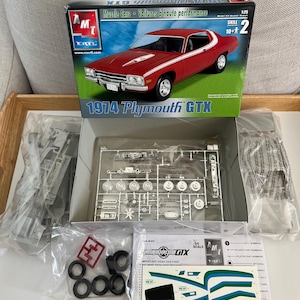 Puede incluir: Un kit de maqueta de coche de carreras Plymouth GTX 1974 a escala 1/25. El kit est&aacute; en su embalaje original e incluye un coche modelo rojo y blanco, una grapa de pl&aacute;stico transparente y una hoja de calcoman&iacute;as. La caja est&aacute; etiquetada con el logotipo de AMT/ERTL y las palabras "Muscle Cars" y "Voitures &agrave; haute performance".