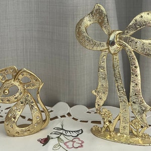 May include: Gold-tone metal earring holder featuring a mouse and a bow design. The holder has multiple holes for earrings.