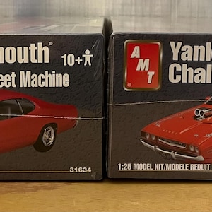 Op de afbeelding: Twee modelbouwsets voor auto's, een is een 1971 Plymouth Duster Street Machine en de andere is een Yankee Challenge. Beide zijn modelbouwsets op schaal 1:25.