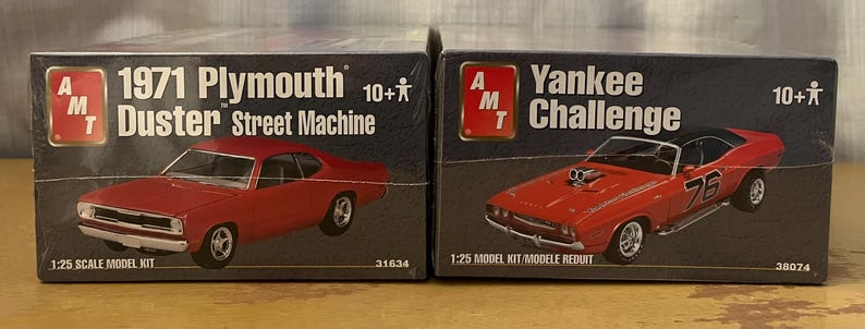 Op de afbeelding: Twee modelbouwsets voor auto's, een is een 1971 Plymouth Duster Street Machine en de andere is een Yankee Challenge. Beide zijn modelbouwsets op schaal 1:25.