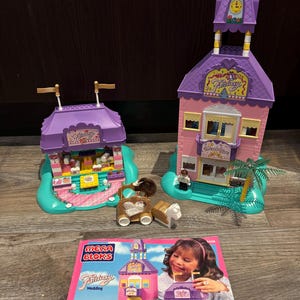 May include: A Mega Bloks Fantasy Wedding playset featuring two buildings, a carriage, a horse, and a figure. The buildings are pink and purple with white trim and display the words "Fantasy Wedding". The set includes instructions.