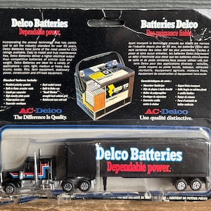 Peut inclure: Un ensemble de jouets camion et remorque Delco Batteries. La remorque noire porte l'inscription "Delco Batteries Dependable power". L'emballage comprend du texte sur les batteries et la marque AC-Delco.