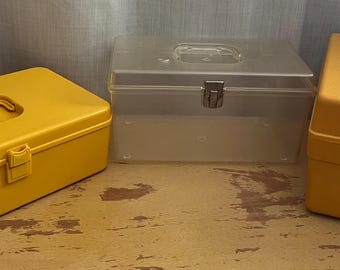 Puede incluir: Tres cajas de almacenamiento de plástico. Dos son amarillas y una es transparente. Las cajas amarillas tienen un asa en la parte superior y un cierre en la parte delantera. La caja transparente tiene un asa en la parte superior y un cierre en la parte delantera.