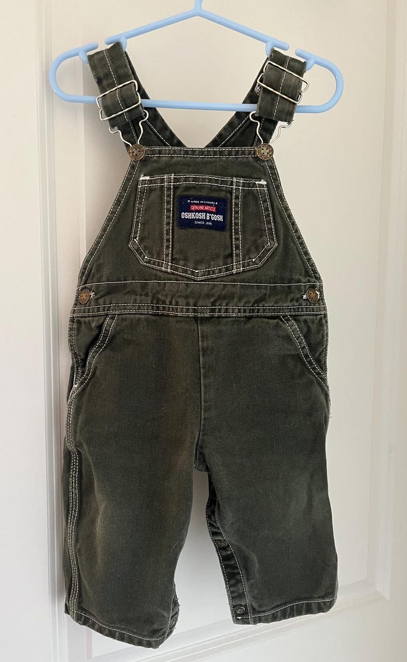 Puede incluir: Pantal&oacute;n vaquero verde con costuras blancas y un parche de logotipo marr&oacute;n OshKosh B'Gosh. El pantal&oacute;n tiene tirantes ajustables con hebillas met&aacute;licas.