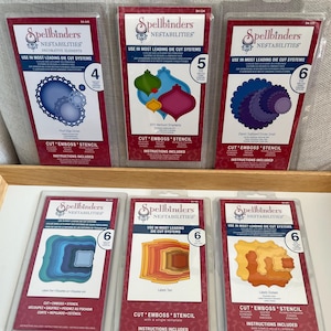 May include: Six Spellbinders Nestabilities die sets for crafting. The sets are packaged in clear plastic boxes with red and white labels. The labels include the Spellbinders logo, the product name "Nestabilities", and the number of dies in each set. The dies are designed for use in most leading die-cut systems. The dies are made of metal and are designed to cut, emboss, and stencil.