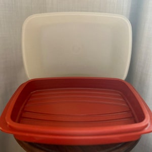 Op de afbeelding: Een rode rechthoekige voedselopslagcontainer met een wit deksel. De container heeft een geribbeld interieur en een iets verhoogde rand. Het deksel is eraf en onthult de binnenkant van de container. De container is gemaakt van plastic.