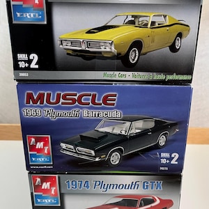 May include: Three model car kits for building 1971 Dodge Charger, 1969 Plymouth Barracuda, and 1974 Plymouth GTX. Each box features a colorful illustration of the car, the car's name, and the manufacturer's logo, AMT Ertl.