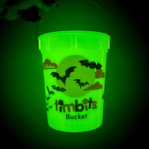 Puede incluir: Un cubo TimBits verde brillante con un diseño de Halloween. El cubo presenta una luna llena, murciélagos y nubes. Las palabras "TimBits" y "Bucket" están impresas en la parte delantera.