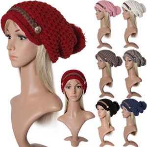 Può includere: Un set di dieci berretti di lana con un pon pon in cima. I berretti sono di vari colori, tra cui rosso, rosa, bianco, grigio, nero e blu. Ogni berretto ha una fascia intrecciata attorno alla base e un bottone sul lato.