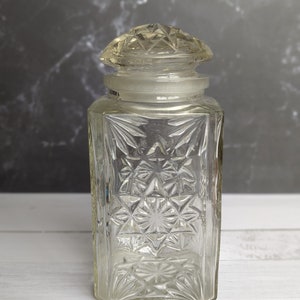 May include: A clear glass jar with a diamond-shaped lid. The jar has a textured, starburst pattern.