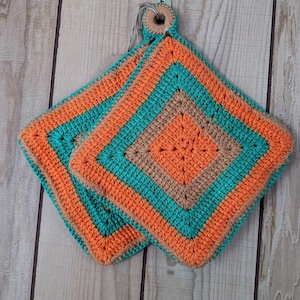 May include: Two crocheted pot holders in orange, brown, and teal. The pot holders are square shaped and have a loop for hanging.