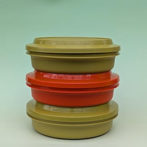 Könnte beinhalten: Stapel von drei Vintage-Kunststoff-Lebensmittelbehältern. Die oberen und unteren Behälter sind olivgrün, der mittlere ist leuchtend rot. Jeder Behälter hat einen passenden Deckel.