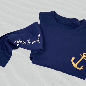 May include: Navy blue long-sleeved shirt with a gold anchor on the front and the text "refuse to sink" on the sleeve.