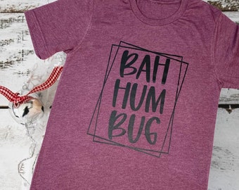 May include: Burgundy colored t-shirt with the text "BAH HUM BUG" in black lettering inside a black box.