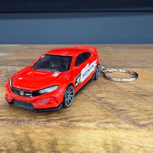 May include: A red Honda Civic Type R model car keyring. The miniature car has black wheels, a detailed front grille, and the Honda logo. The keyring is attached to a silver metal ring.