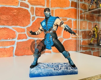 May include: A detailed action figure of a ninja character wearing a blue and black tunic with a matching mask and arm guards. The figure stands in a dynamic combat pose on a textured blue base that resembles ice, with visible straps and buckles.