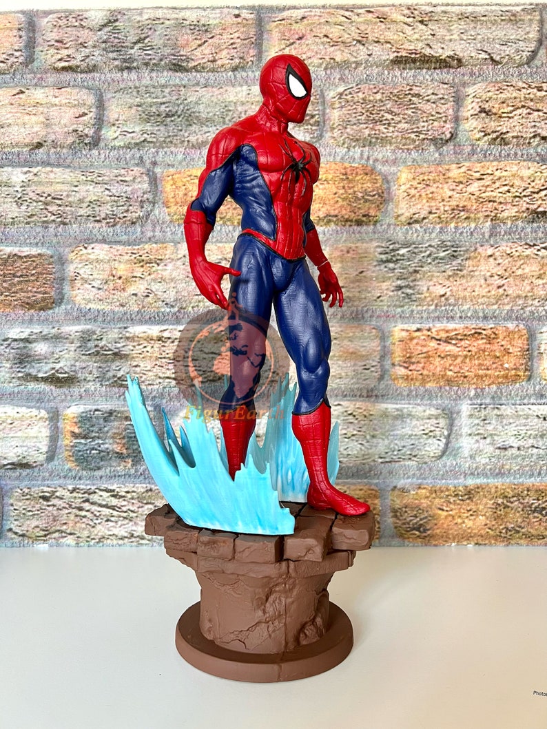 May include: A red and blue Spider-Man action figure stands on a brown stone base with blue and white web-like effects. The figure is posed with one arm raised and the other at its side.