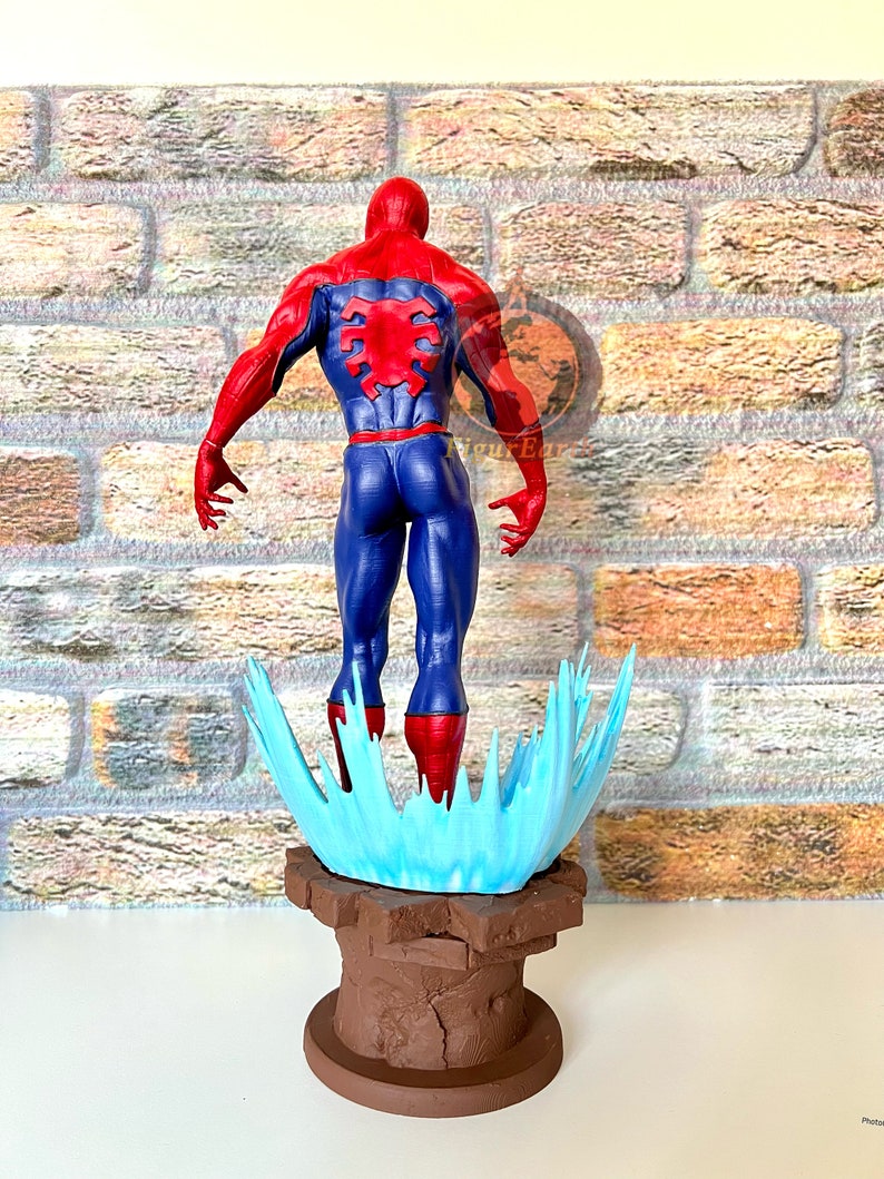 May include: A red and blue action figure of Spider-Man standing on a blue and brown base. The figure is posed with its back to the viewer, and its arms are outstretched.