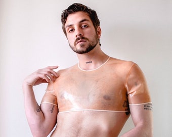May include: A nude-colored, transparent crop top with short sleeves and a matching thong. The top has a crew neck and a horizontal band across the chest. The thong features a low-rise design with a metallic detail.