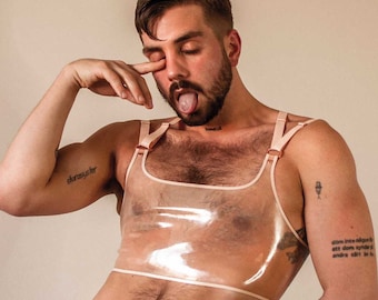 May include: A transparent, blush-toned top with thin straps and a square neckline. The top is worn by a person with a beard and tattoos. The overall aesthetic is modern and minimalist, with a focus on the garment's design and texture.