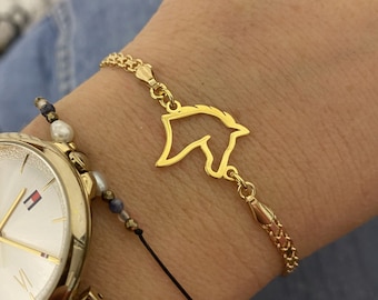 May include: A gold chain bracelet with a delicate horse head charm. The bracelet is on a person's wrist, along with a black string bracelet and a gold watch.