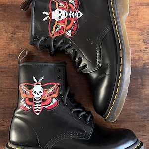 May include: Black leather boots with yellow stitching and a skull and butterfly design painted on the side.