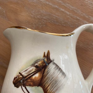Pode incluir: Jarro de cer&acirc;mica branca com uma borda dourada e uma imagem pintada de uma cabe&ccedil;a de cavalo marrom com uma r&eacute;dea.