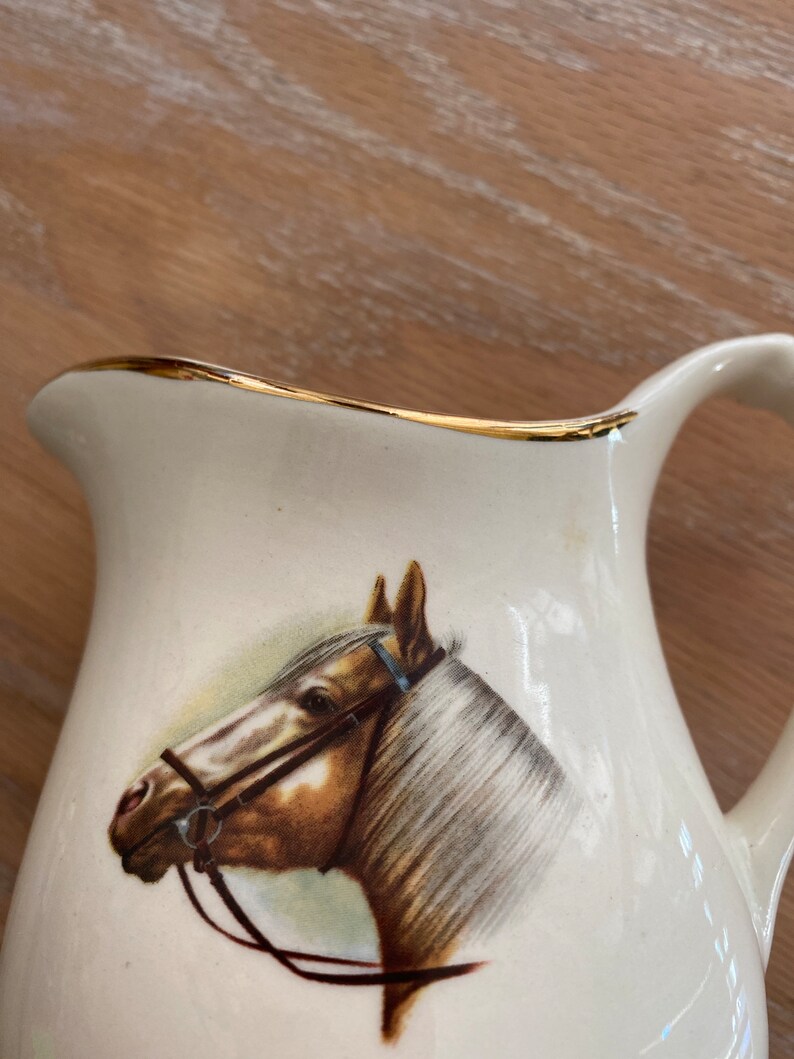Pode incluir: Jarro de cer&acirc;mica branca com uma borda dourada e uma imagem pintada de uma cabe&ccedil;a de cavalo marrom com uma r&eacute;dea.