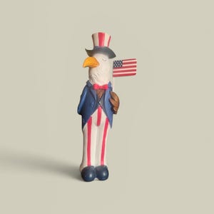May include: A patriotic figurine of an eagle dressed as Uncle Sam, holding a small American flag. The eagle wears a top hat, blue jacket, red bow tie, and striped pants. The figurine is painted in red, white, blue, and brown.