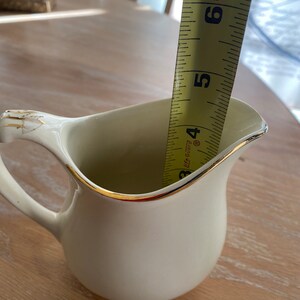 Pode incluir: Um cremoso de cer&acirc;mica branca com uma borda dourada, medido com uma fita m&eacute;trica amarela que diz "Made in U.S.A." e tem marcas at&eacute; 15 cm.