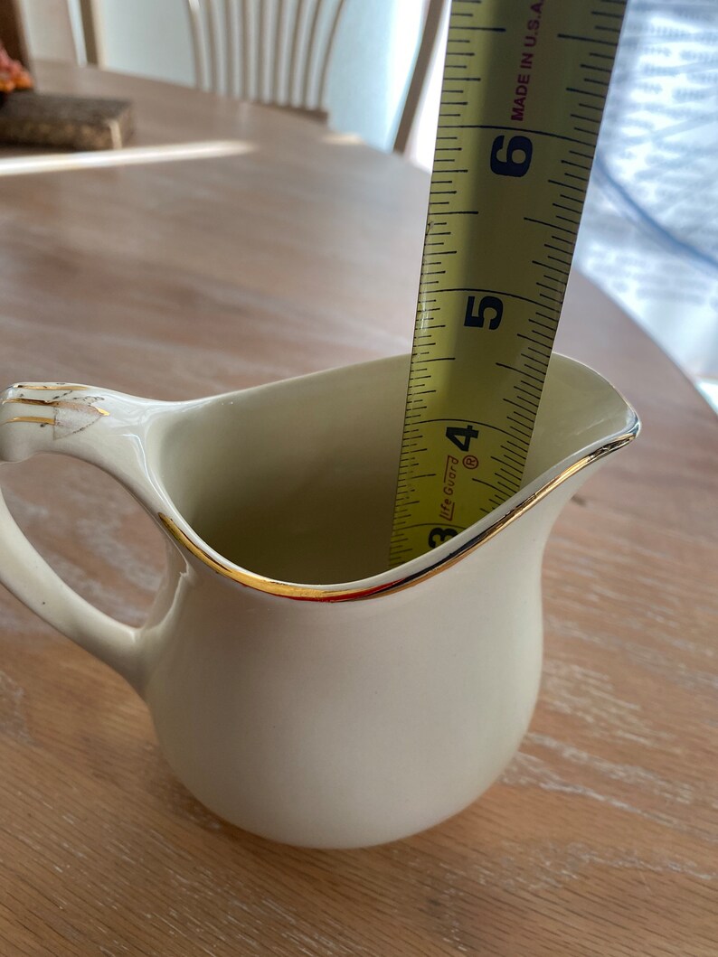 Pode incluir: Um cremoso de cer&acirc;mica branca com uma borda dourada, medido com uma fita m&eacute;trica amarela que diz "Made in U.S.A." e tem marcas at&eacute; 15 cm.