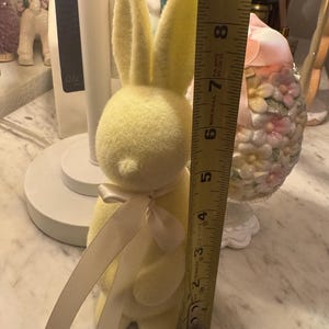 Może przedstawiać: Żółty pluszowy królik z białą satynową kokardką. Królik ma około 18 cm wysokości.