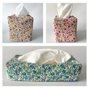 May include: Three fabric tissue box covers with floral designs. Two are square, one with yellow, purple, and red flowers, the other with pink flowers. The third is rectangular with blue and green flowers. Each has white tissues.