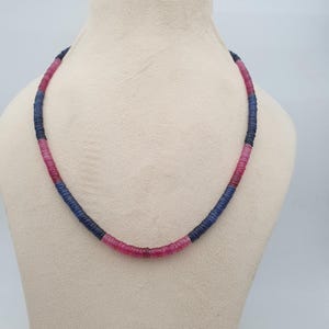 May include: A necklace composed of small, round beads in shades of pink and blue. The beads are strung together to form a continuous strand. The necklace is displayed on a mannequin, showcasing its design and color variations.