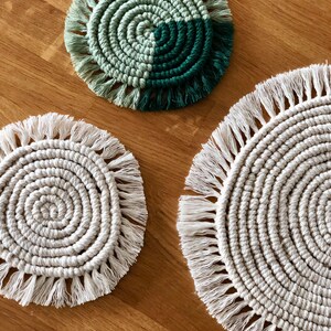 May include: Three round crocheted coasters with fringe. One coaster is green and white, and the other two are white.
