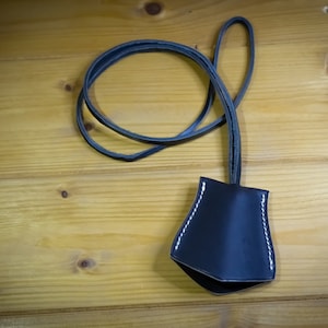 May include: A black leather key chain with a small pouch and a white stitching detail. The key chain is on a wooden surface.