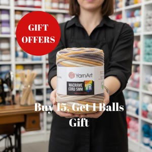 May include: A large spool of YarnArt Macrame Cord 5mm in neutral tones of beige, tan, and gray is held by a person. The label reads "Macrame Cord 5mm VR". A red circle with white text reads "GIFT OFFERS". The text "Buy 15, Get 1 Balls Gift" is also visible.