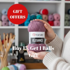 May include: A close-up of a ball of YarnArt Elegance yarn in a dusty rose color. The label reads "Elegance" and "Buy 15, Get 1 Balls Gift". A red circle with the words "GIFT OFFERS" is in the upper left corner. Shelves of yarn are in the background.