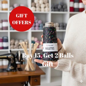 May include: A black yarn spool with colourful sequins is held in front of a shelf filled with yarn. The spool has a label that reads "PAILLETTES". A red circle with the words "GIFT OFFERS" is in the upper left corner. The text "Buy 15, Get 2 Balls Gift" is at the bottom.