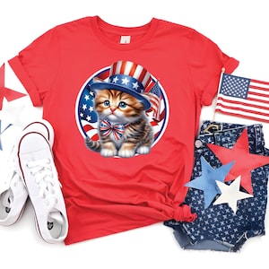May include: A red t-shirt featuring a patriotic kitten wearing a top hat and bow tie, with an American flag design. The image includes white sneakers and denim shorts with star patterns, perfect for Independence Day celebrations.